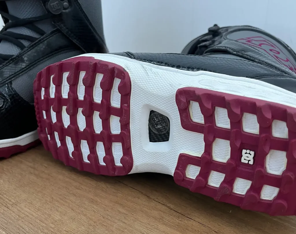 Close-up of the DC Misty snowboard boot outsole, showing the burgundy tread pattern and white midsole on a wooden floor.