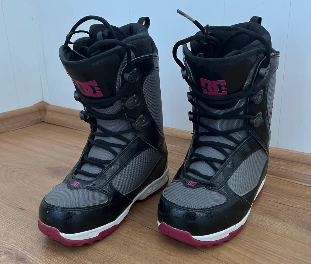 Pair of DC Misty women’s snowboard boots (2011 model) in black and grey with pink DC logos, standing on a wooden floor.