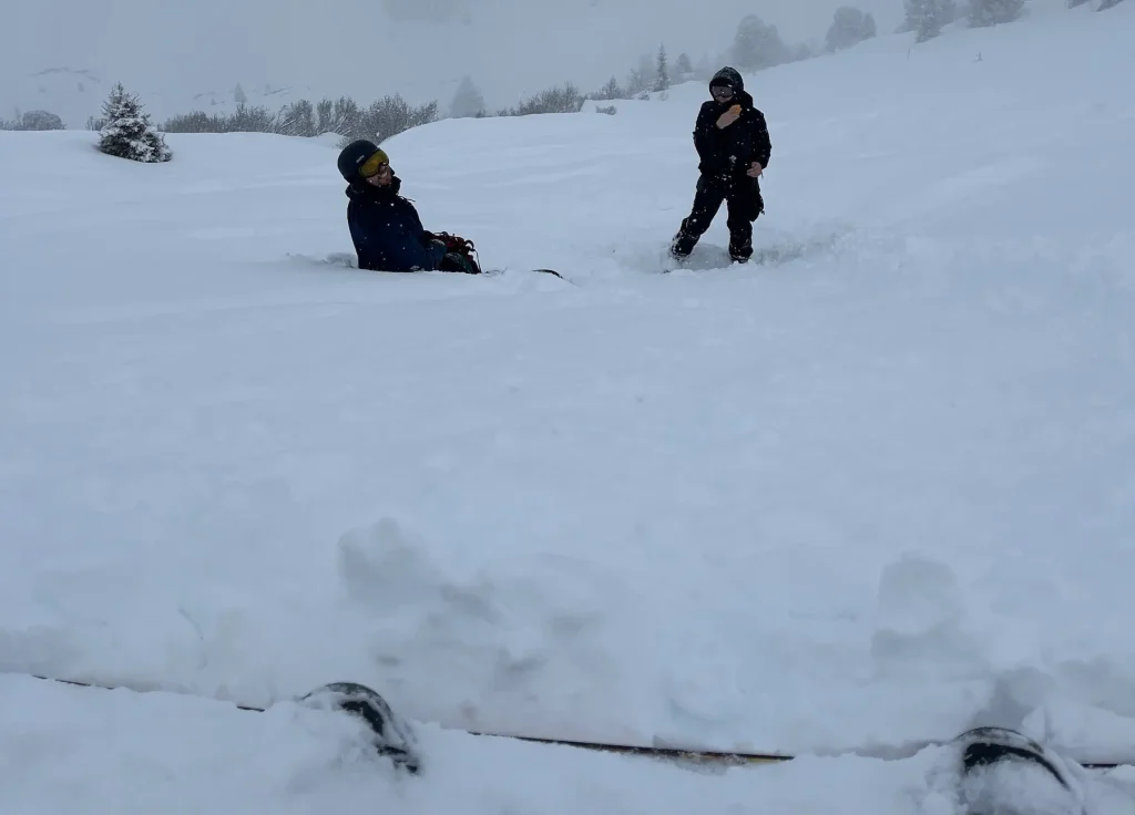 Two snowboarders in deep powder during a snowy freeride day in Austria, with one sitting half-buried in snow while the other stands nearby.